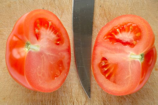 Tomato and blade on brown wooden chopping board