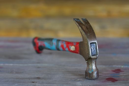 Old colorful iron hammer on wooden table with spots of paint. Tool work