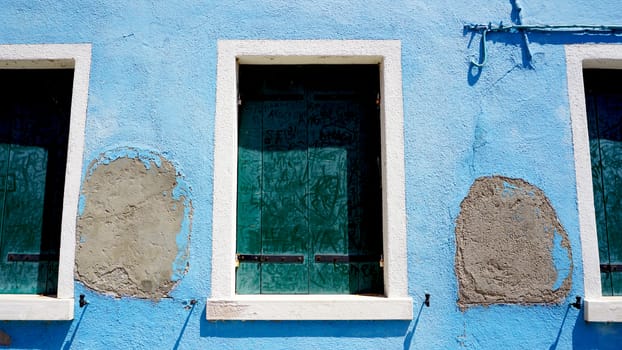 three Windows in Burano on decay blue wall building architecture, Venice, Italy