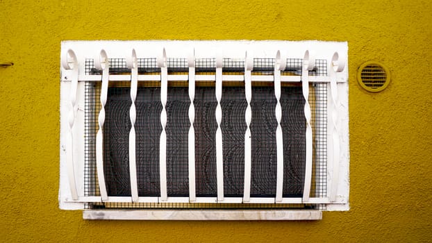 Window on yellow mustard wall building in Burano, Venice, Italy