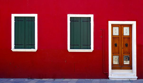 wooden door and two windows on red color wall in Burano, Venice, Italy