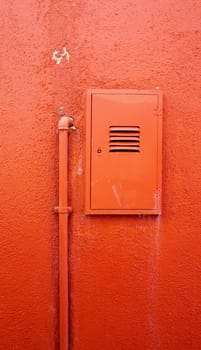 vertical metal pipe and electric box on orange color wall in Burano, Venice, Italy