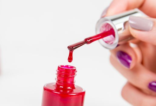 Red nail polish dropping in nail polish bottle on white background