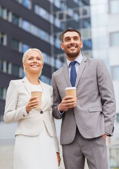 business, partnership, hot drinks and people concept - smiling businessmen with paper cups standing over office building