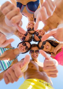 friendship, summer vacation, holidays, gesture and people concept - group of smiling friends wearing swimwear standing in circle and showing thumbs up over blue sky