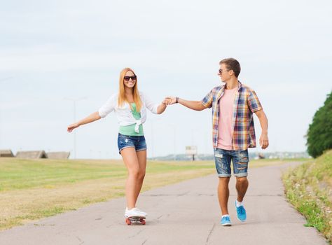 holidays, vacation, love and friendship concept - smiling couple with skateboard riding and holding hands outdoors