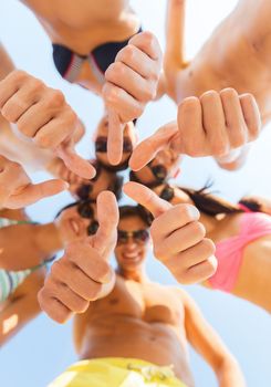 friendship, summer vacation, holidays, gesture and people concept - close up of smiling friends wearing swimwear standing in circle and showing thumbs up over blue sky