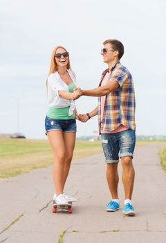 holidays, vacation, love and friendship concept - smiling couple with skateboard riding and holding hands outdoors