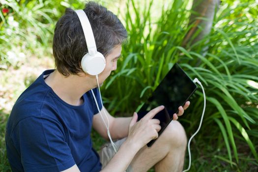 young man holding a tablet with headphones, outdoor