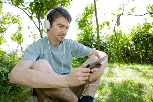 young man holding a tablet with headphones, outdoor