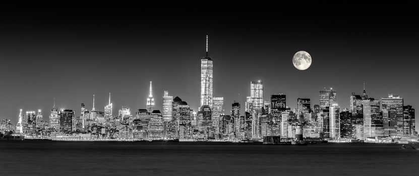 New York City Manhattan downtown skyline at dusk with skyscrapers illuminated over Hudson River panorama. Horizontal composition, copy space. Black and white image.