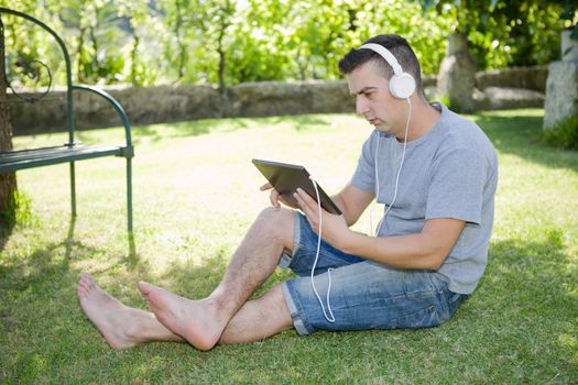 young man holding a tablet with headphones, outdoor