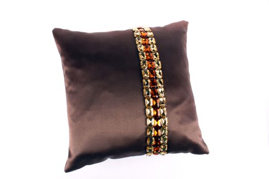 A brown pillow with a beautiful design on its cover, on white studio background.