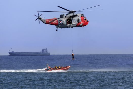 A Royal Navy Sea King Search and Rescue helicopter lifting a casualty from a small boat in a busy shipping lane off the northeast coast of the United Kingdom.