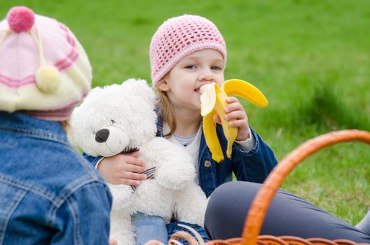 The three-year child eats banana on a picnic on the green lawn