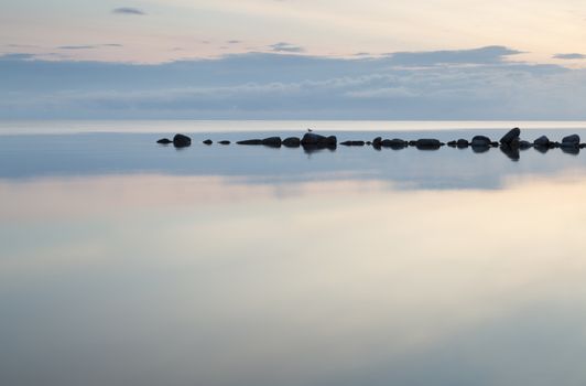 Breakwater Rocks in Calm Sea with clouds and reflextions in the water.