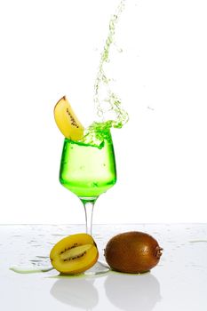 Stemmed champagne glass with kiwi liquor splashing out, isolated on white background