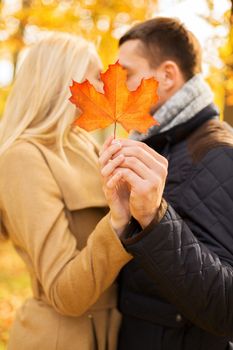 love, relationship, family and people concept - close up of couple with maple leaf kissing in autumn park