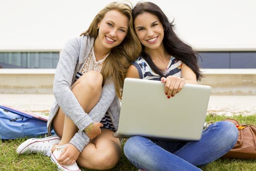 Tennage students sitting on the grass and study together with a laptop