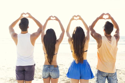 Group of friends together at the beach and making hearth shapes with her hands