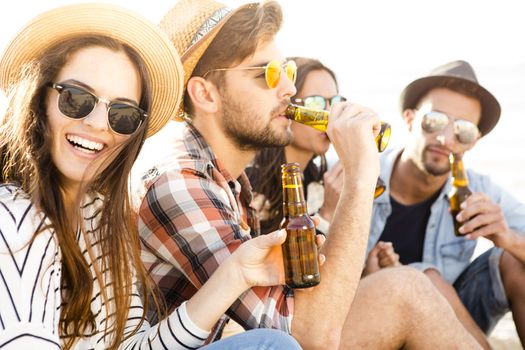 Friends having fun together at the beach and drinking a cold beer