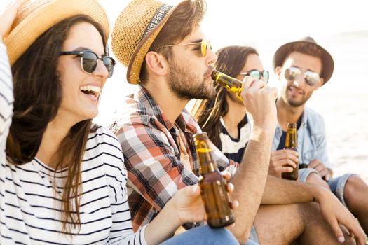 Friends having fun together at the beach and drinking a cold beer