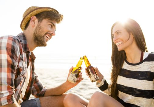 Young couple at the beach having fun, laughing and drinking beer