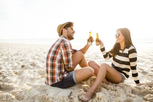 Young couple at the beach having fun, laughing and drinking beer