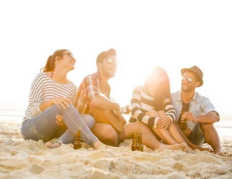 Friends having fun together at the beach, playing guitar and drinking beer