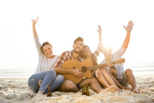 Friends having fun together at the beach, playing guitar and drinking beer