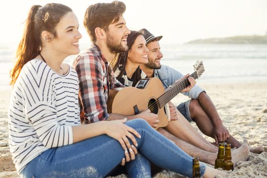 Friends having fun together at the beach, playing guitar and drinking beer