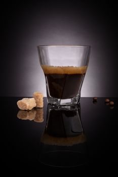 Espresso in glass with coffee beans and crane sugar cubes on dark background. Gourmet luxurious coffee drinking.