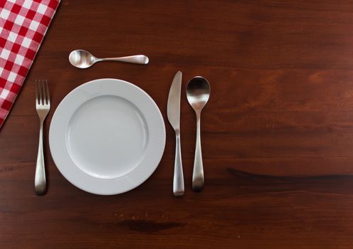 empty white plate with cutlery over wooden table