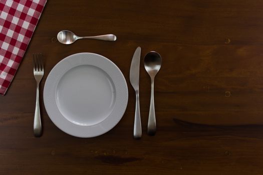 empty white plate with cutlery over wooden table