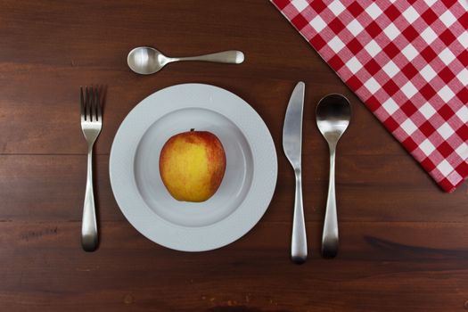 white dish with cutlery and apple in the center of wooden table