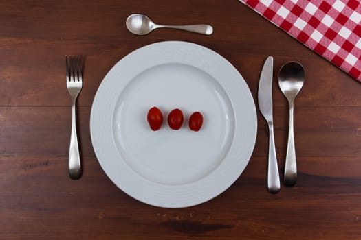 white plate with tomatoes on wooden table with cutlery