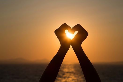 Silhouettes hand heart shaped with sun sets and the sky orange