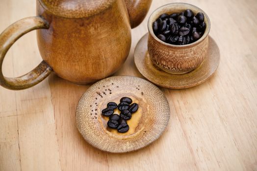 Coffee beans, cup of coffee and teapot on wooden desk. Set of cafe