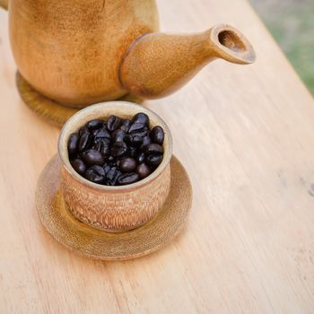 Coffee beans, cup of coffee and teapot on wooden desk. Set of cafe