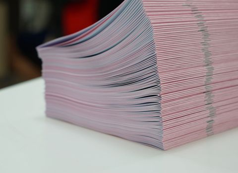 Piles of pink handout papers placed on table at office.                            