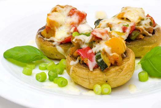 Mushrooms stuffed with vegetables and cheese on white plate fork and knife