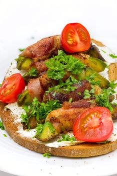 A slice of toasted bread with avocado wrapped with bacon on white plate