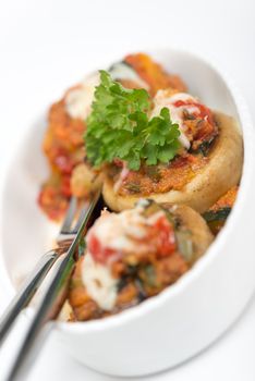 Mushrooms stuffed with vegetables and cheese on white plate fork and knife