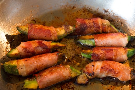 fried avocado pieces wrapped in bacon in a pan