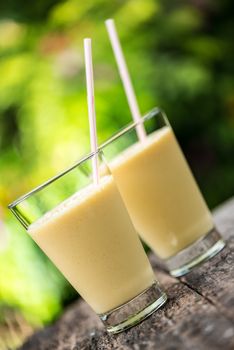 Fresh homemade mango  smoothie in a glass, served outside in a garden on a wood table