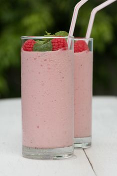 Fresh homemade raspberry smoothie in a glass, served outside in a garden on a white wood table