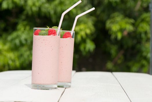 Fresh homemade raspberry smoothie in a glass, served outside in a garden on a white wood table