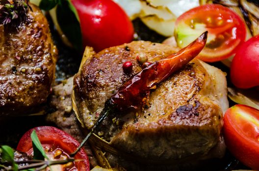 Closeup of pork tenderloin medallions with onion tomatoes garlic and pepper in a pan