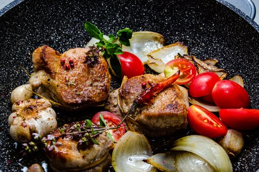 Closeup of pork tenderloin medallions with onion tomatoes garlic and pepper in a pan