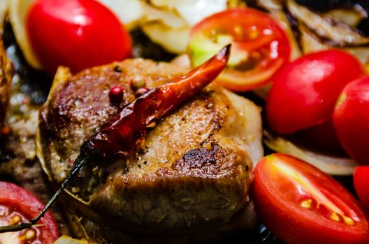 Closeup of pork tenderloin medallions with onion tomatoes garlic and pepper in a pan